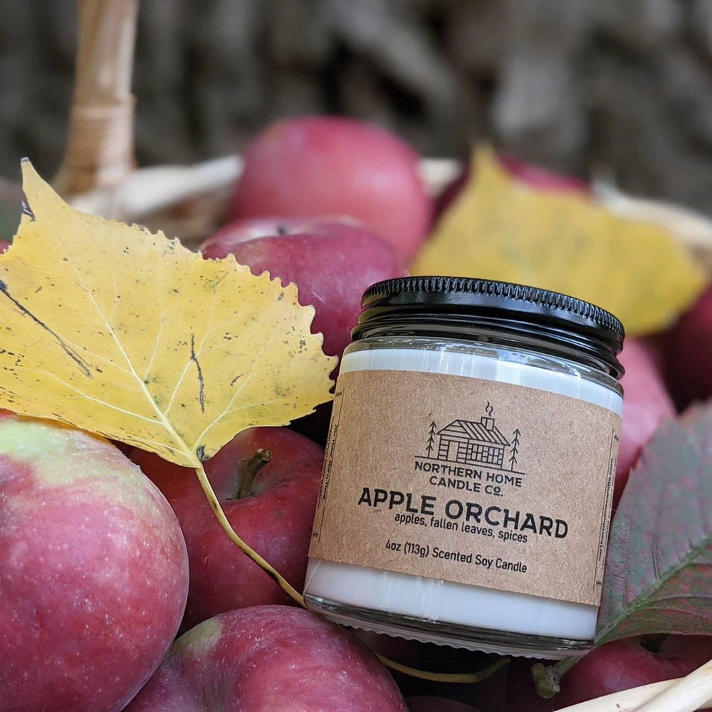 Soy candle with brown label that reads northern home candle company apple orchard surrounded by apples and leaves.