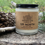 8 ounce soy candle with brown label that reads northern home candle and up north. Pine cones, birch bark, and pine needles are in the background.