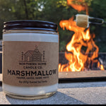 8 Ounce Soy Candle in Clear Jar with Brown Northern Home Candle Company label that reads marshmallow. Fire and roasted marshmallow in the background.
